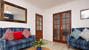 Una sala de estar con dos sofás azul y blanco a cuadros, una mesa de centro de madera, una planta en maceta y un espejo grande en la pared.