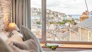 A bedroom with a large window overlooking a colorful town. - 2 Bed in Brixham (oc-s27146) (Brixham)