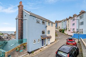 Une rue résidentielle bordée de maisons mitoyennes, avec un ciel dégagé et des voitures garées.