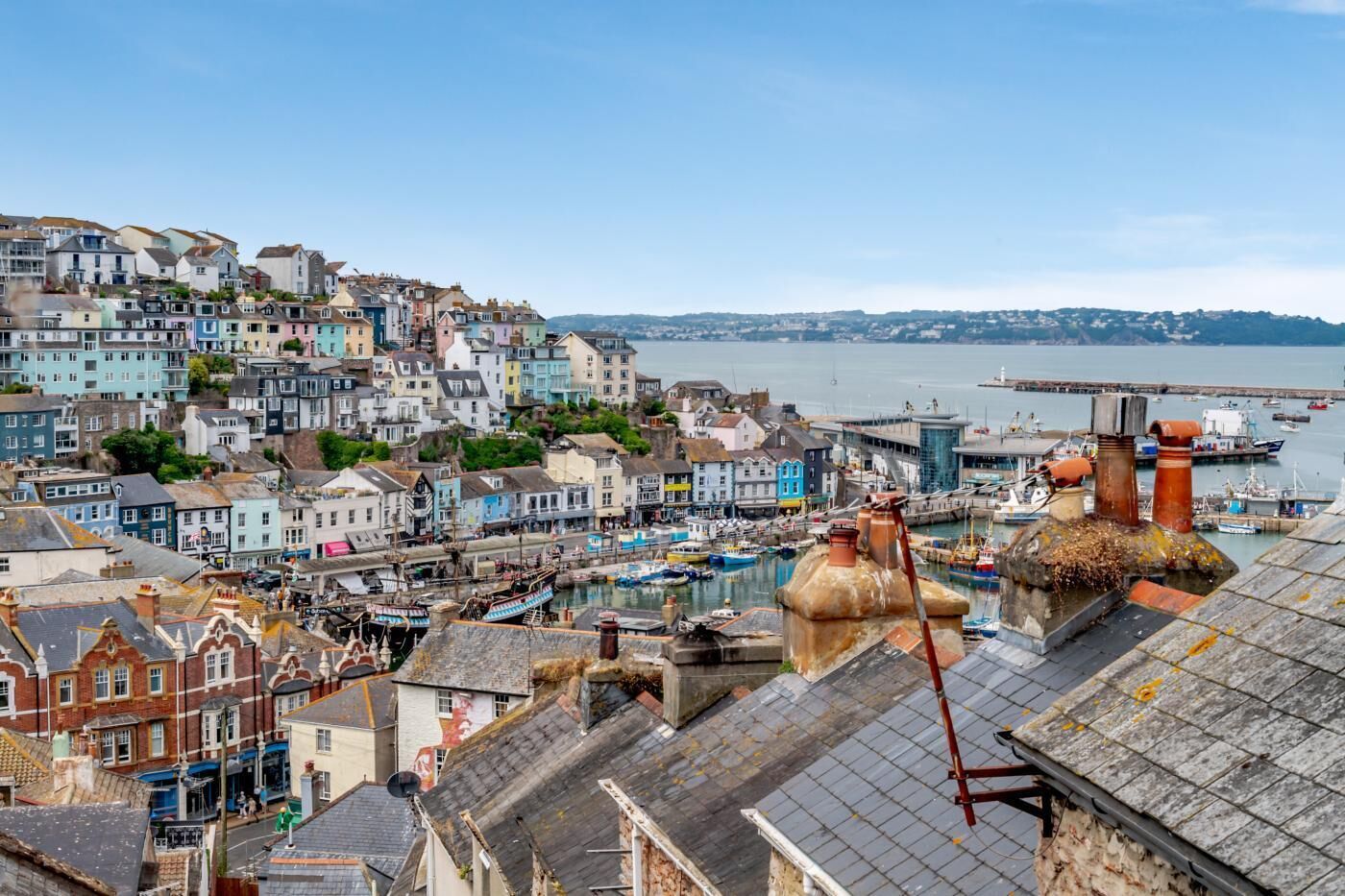 Une ville côtière aux bâtiments aux couleurs vives, un port où sont amarrés des bateaux et une cheminée imposante qui la domine.