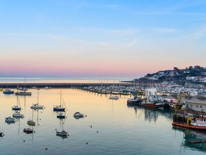 Un port de plaisance avec des bateaux amarrés, une jetée s’avançant dans l’eau et, au loin, une ville perchée sur une colline.