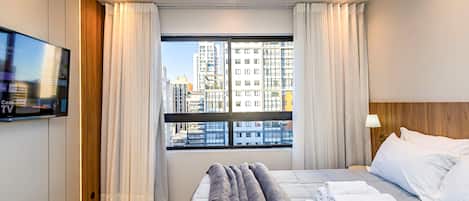 A hotel room with a bed, a TV, a window with curtains, and a city view.