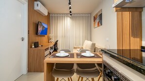 A modern kitchen with a dining area, a TV mounted on the wall, and a built-in oven. - MUV Residence (Curitiba)