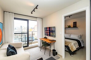 Eine moderne Wohnung mit Balkon, Essbereich, Bett und einem großen Fenster.