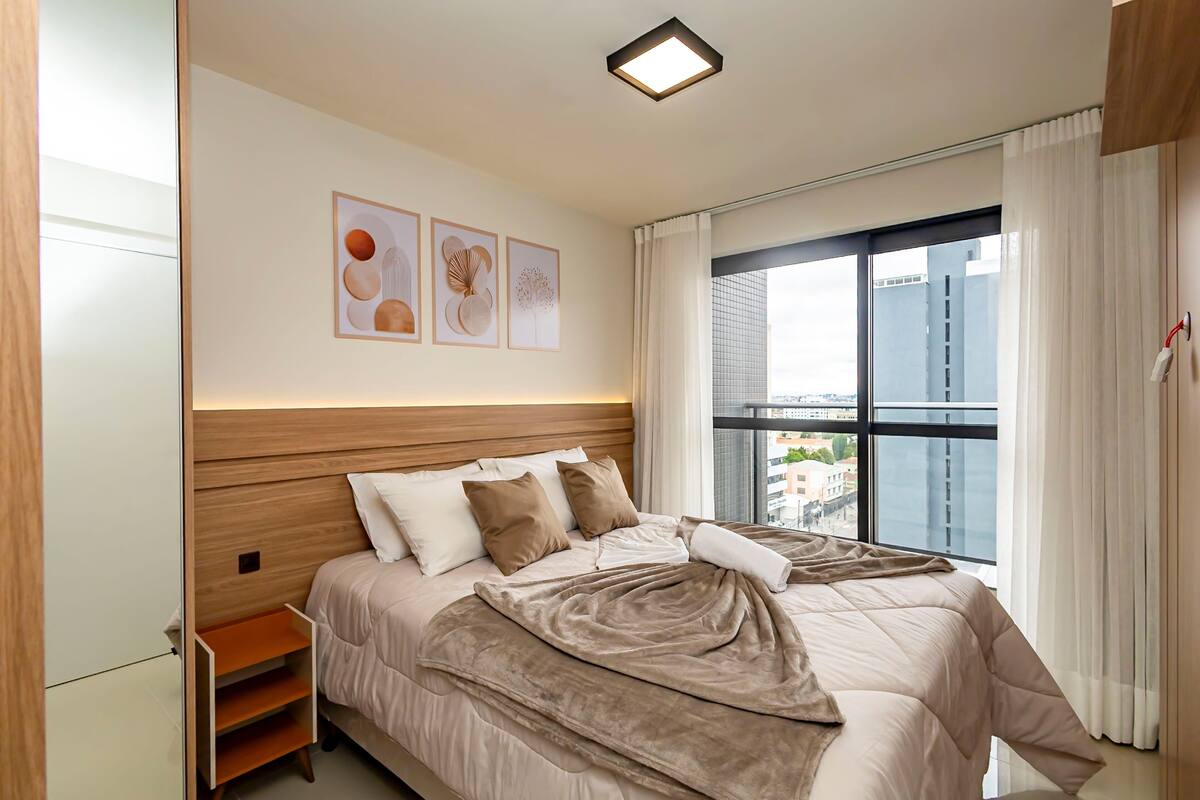 Habitació d'hotel moderna amb un llit gran, una taula de nit, una finestra amb cortines i una obra d'art a la paret.