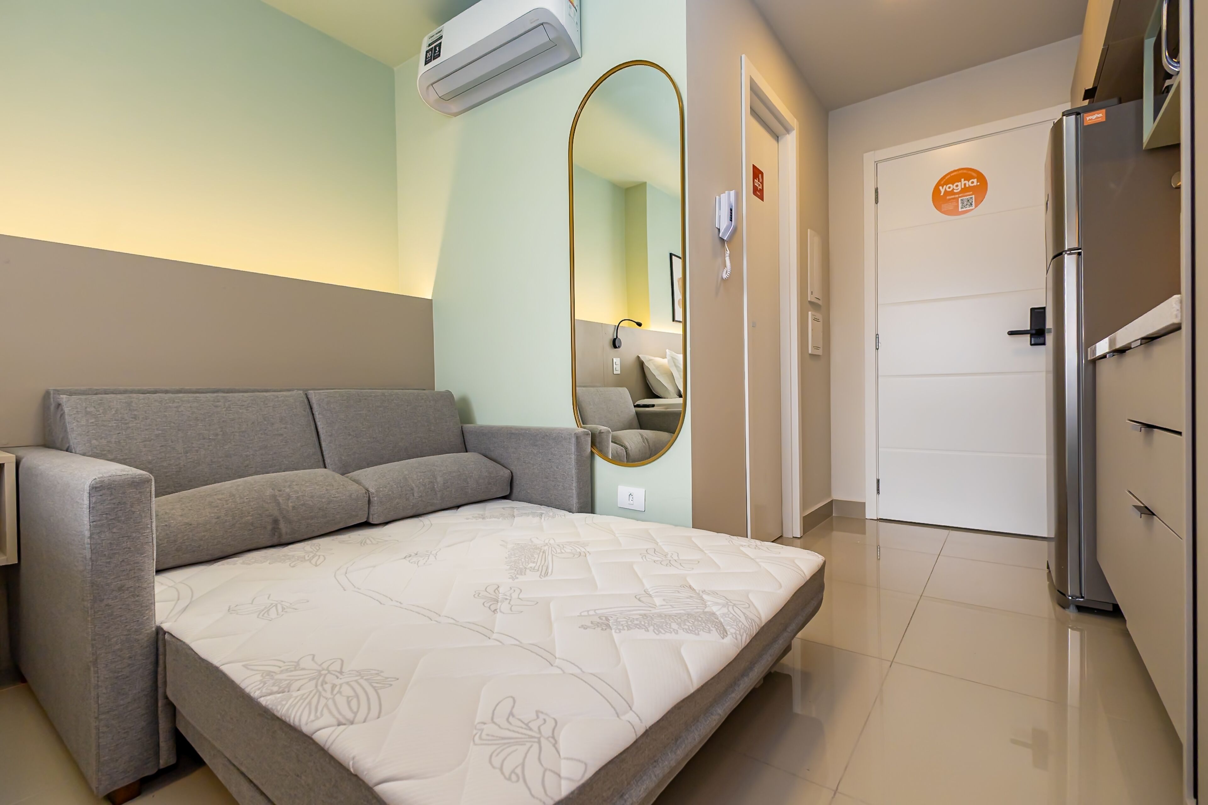 Ein Hotelzimmer mit Schlafsofa, Spiegel, einer Tür mit Schild und einem Kühlschrank.