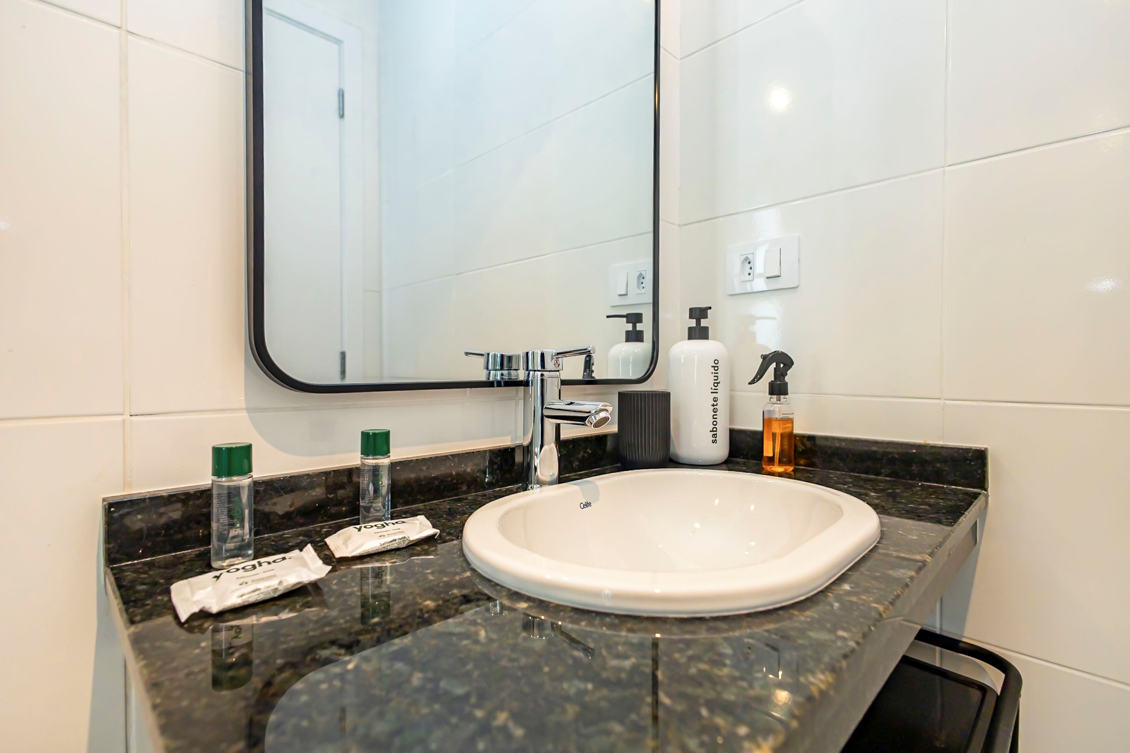 A bathroom with a white sink, a mirror, and toiletries on the counter.