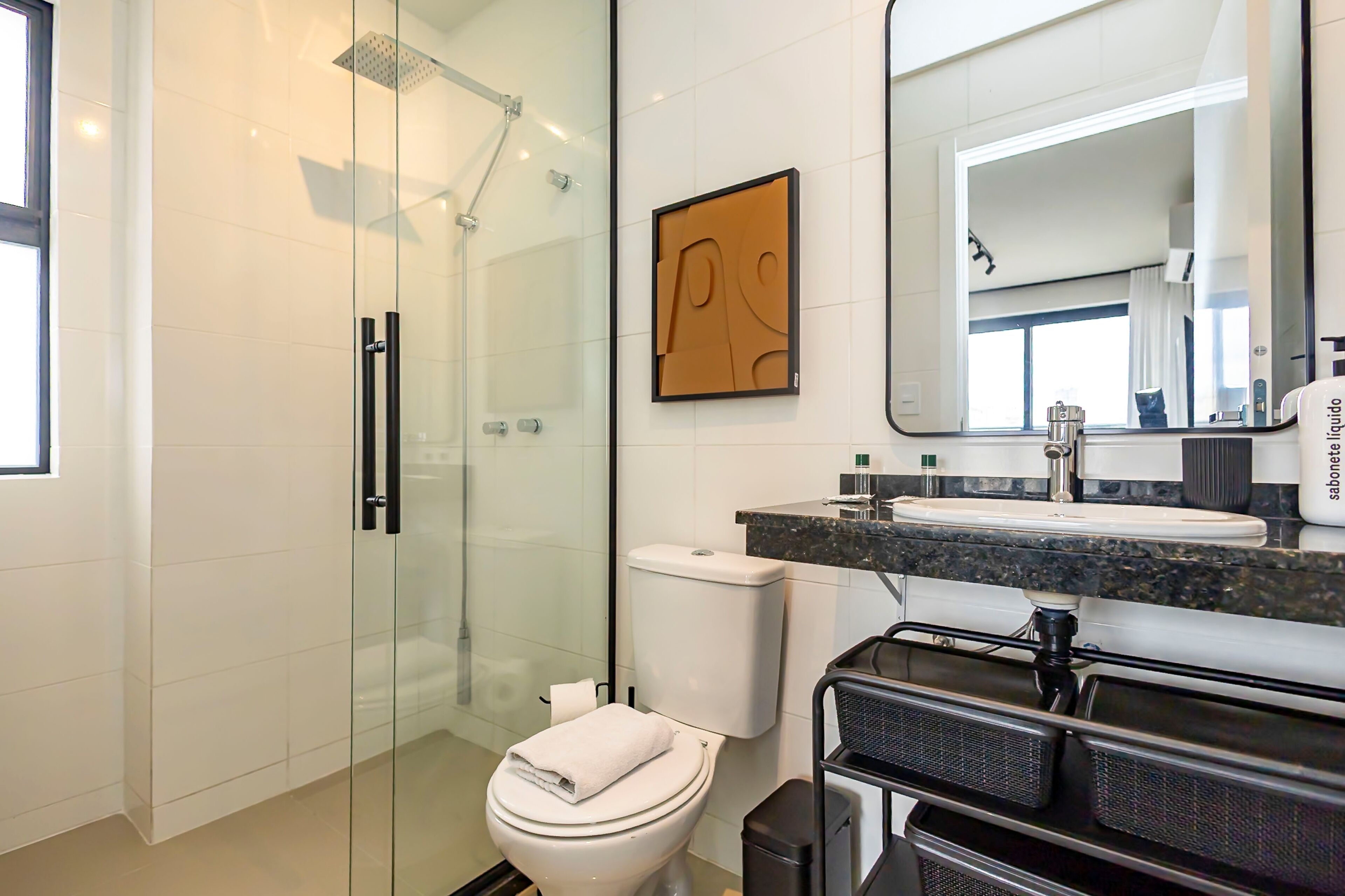 Un baño moderno con cabina de ducha de vidrio, inodoro, lavamanos con encimera de mármol y un espejo grande.