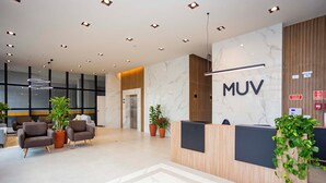 A modern reception area with a wooden reception desk, a marble floor, and potted plants. - MUV Residence (Curitiba)