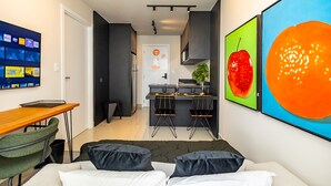 A modern hotel room with a bed, a desk, a chair, a small kitchen area, and artwork on the walls. - MUV Residence (Curitiba)