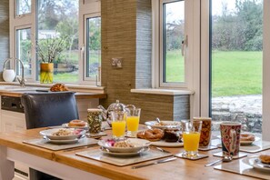 A breakfast table with plates, glasses of orange juice, a teapot, and a vase with flowers. - 10 Bed in Llanrhidian (oc-s27225) (Pen-clawdd)