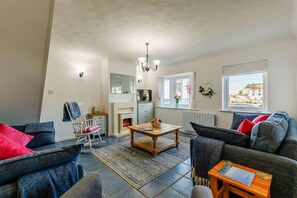 A living room with a fireplace, a dining table, and a sofa. - 3 Bed in Porthleven (oc-1seav) (Porthleven)
