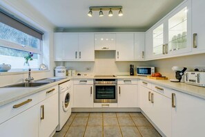A modern kitchen with white cabinets, stainless steel appliances, and a window with a view. - 3 Bed in Porthleven (oc-1seav) (Porthleven)