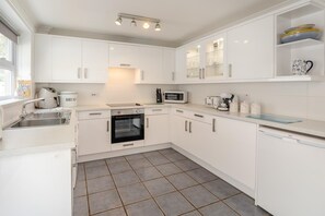 A modern kitchen with white cabinetry, a built-in oven, a microwave, and a coffee maker. - 3 Bed in Porthleven (oc-1seav) (Porthleven)