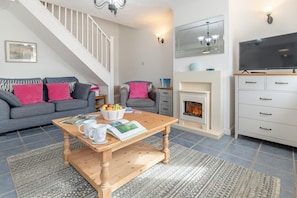 A living room with a fireplace, a sofa, a coffee table with magazines, and a television. - 3 Bed in Porthleven (oc-1seav) (Porthleven)