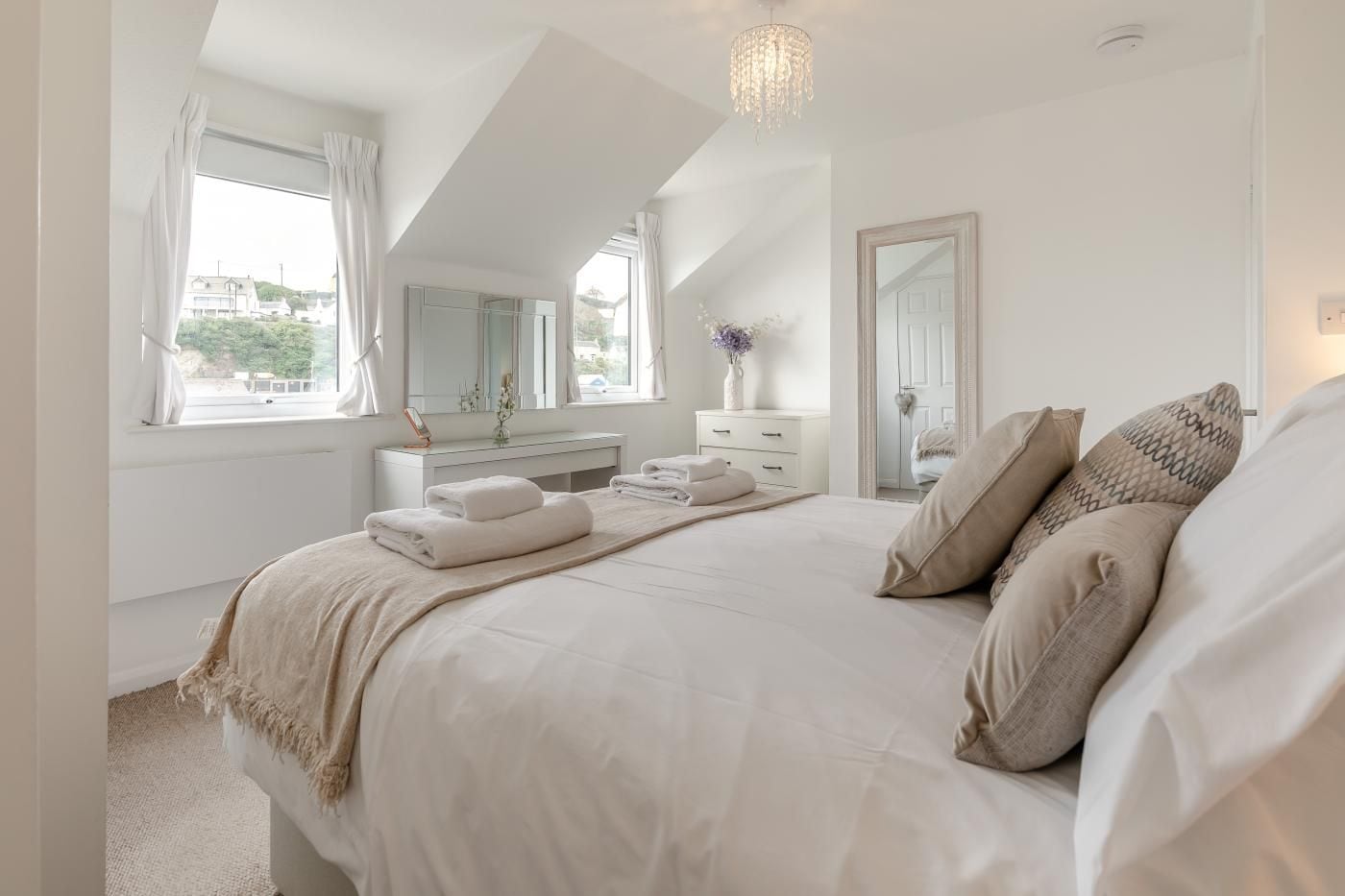 A bedroom with a large bed, a dresser, a mirror, and a chandelier.