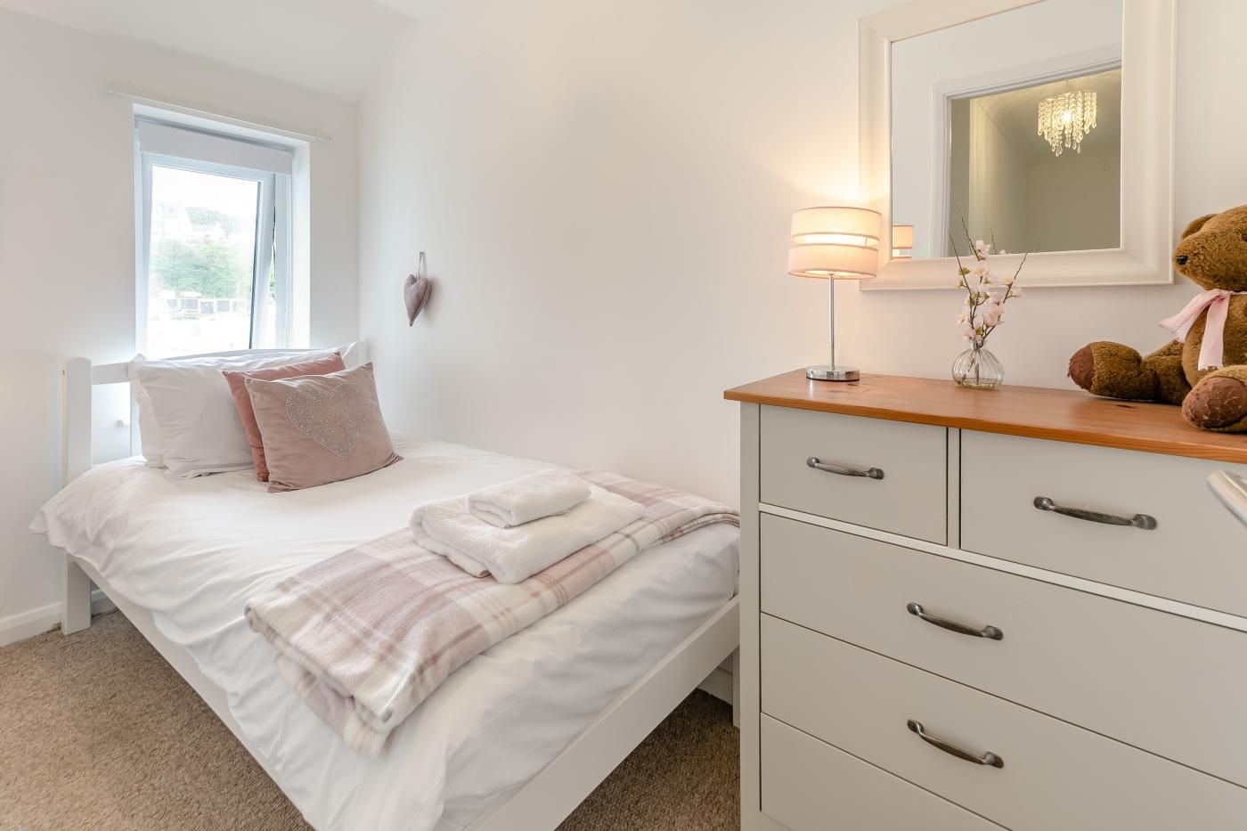 Une chambre à coucher avec un lit, une table de chevet, une lampe, un miroir et un ours en peluche.