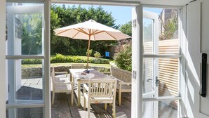 Eine offene Terrasse mit Tisch und Stühlen, einem großen Sonnenschirm und Blick auf einen Garten.