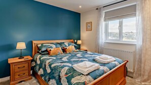 Ein Schlafzimmer mit Bett, Nachttischen, einem Fenster mit Vorhängen und Blick ins Freie.