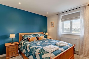 Quarto com cama, mesas de cabeceira, janela com cortinas e vista para o exterior.
