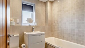 A bathroom with a toilet, sink, mirror, and bathtub. - 3 Bed in St. Austell (oc-t27271) (London Apprentice)
