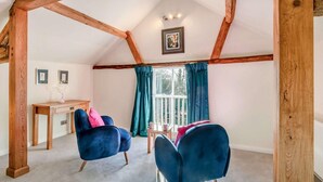 A cozy room with a sloped ceiling, wooden beams, a desk, two blue chairs, and a window with curtains. - 1 Bed in Eye (oc-tch1) (Eye)