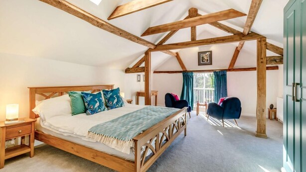 A bedroom with a wooden bed, a nightstand, a chair, and a view of the outdoors through a window. - 1 Bed in Eye (oc-tch1) (Eye)
