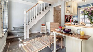 A modern kitchen with a wooden staircase, a dining area with a table set for breakfast, and a view of the outside through a window. - 1 Bed in Yoxford (oc-c27254) (Wickham Market)
