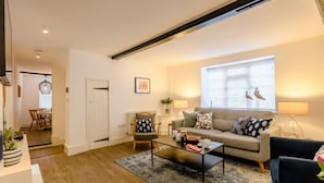 A modern living room with a sofa, coffee table, and chairs. There is a dining area in the background and a window with blinds. - 2 Bed in Holt (oc-c27160) (Holt)