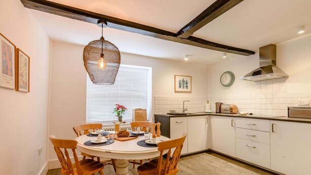 A modern kitchen with white cabinets, a round dining table with chairs, and a hanging light fixture. - 2 Bed in Holt (oc-c27160) (Holt)