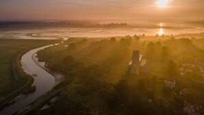 Une rivière serpente à travers un paysage où se dressent une imposante structure en forme de tour et quelques bâtiments, le tout sous un ciel dégagé.