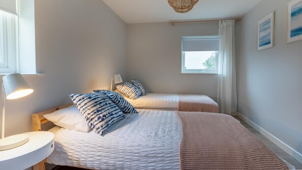 Une chambre avec deux lits, une lampe de chevet, une fenêtre avec des rideaux et un luminaire suspendu.