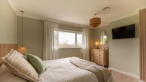 Une chambre à coucher avec un lit, une commode, un téléviseur et une fenêtre avec des rideaux.