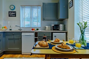 Eine moderne Küche mit Geschirrspüler, Mikrowelle und Toaster. Es gibt eine Frühstücksecke mit Croissants, Saft und einem Blumentopf mit Grünpflanzen.