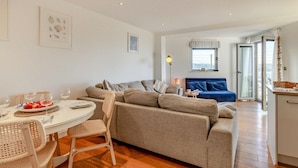 A modern living room with a grey sofa, a dining table with chairs, and a blue sofa in the background. - 2 Bed in Newquay (oc-a27276) (Newquay)