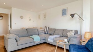 A modern living room with a grey sectional sofa, a small round table with a plate and cup, a floor lamp, and a blue armchair. - 2 Bed in Newquay (oc-a27276) (Newquay)
