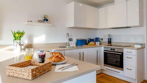A modern kitchen with white cabinets, a built-in oven, and a countertop with breakfast items. - 2 Bed in Newquay (oc-a27276) (Newquay)