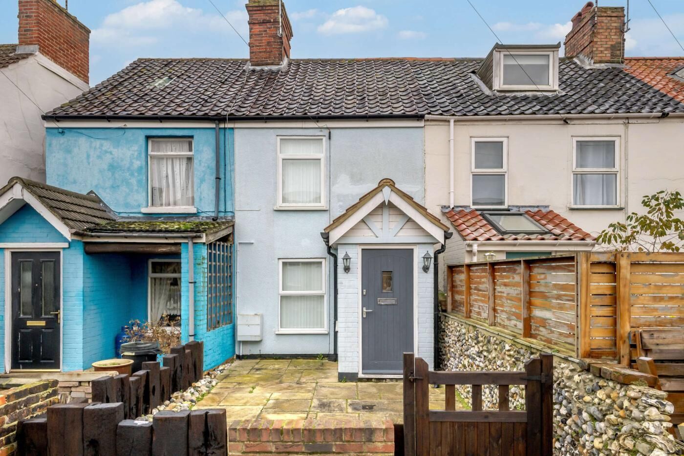 A row of terraced houses with a small courtyard, a wooden gate, and a stone wall.