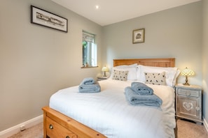 A neatly made bed with white bedding and two rolled towels, a wooden nightstand with a lamp, and a framed picture on the wall. - 3 Bed in Baslow (oc-h27288) (Baslow)