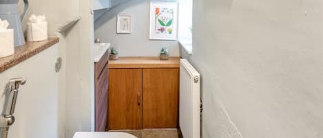 Une petite salle de bain avec des toilettes blanches, des meubles en bois, un radiateur et une petite étagère contenant des articles de toilette.