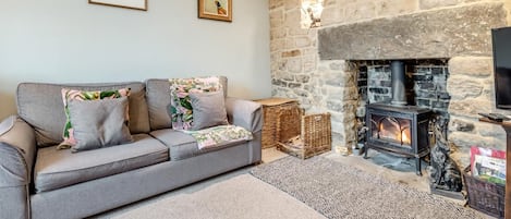 A cozy living room with a stone fireplace, a grey sofa, and two framed pictures on the wall.