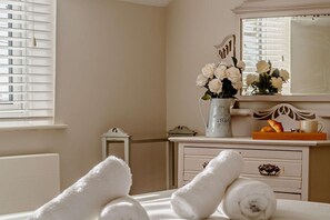 A bedroom with a bed, a dresser, a mirror, a vase of flowers, and a window with blinds.