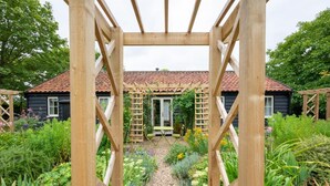 A wooden pergola structure in a garden with a tiled roof house in the background. - 3 Bed in Wilby (oc-slowlo) (Wilby)