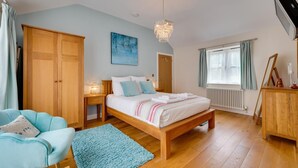 A bedroom with a wooden bed, a blue armchair, a wooden dresser, and a chandelier. - 3 Bed in Wilby (oc-slowlo) (Wilby)