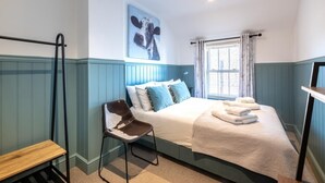 Une chambre à coucher avec un lit, une chaise, une fenêtre avec des rideaux et un tableau accroché au mur.