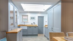 Une cuisine compacte avec des meubles gris, un plan de travail en bois, un puits de lumière et un coin repas comprenant une table et des chaises.