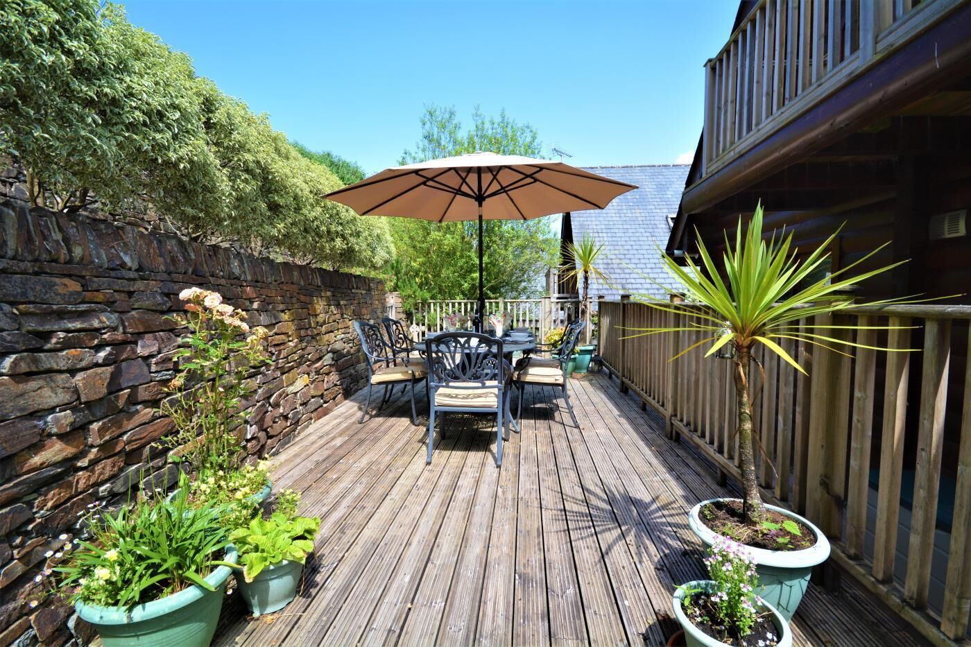 A wooden deck with a table and chairs, an umbrella, and potted plants.