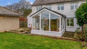 Ein zweistöckiges Haus mit Wintergarten, einer Holzterrasse und einem gepflegten Rasen.