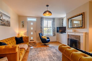 A living room with a sofa, armchair, fireplace, TV, and a door with frosted glass panels. - 3 Bed in Thurne (oc-t27347) (Ashby with Oby)