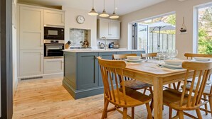 A modern kitchen with a central island, wooden chairs, and a dining table set for four. - 3 Bed in Southwold (oc-s27351) (Southwold)